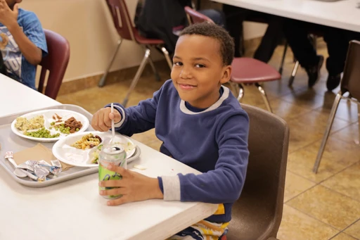 A young boy sitting at a table with a plate of food at the Open Door Mission.