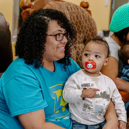 A woman with a baby sitting in a chair receiving assistance from volunteers at Open Door Mission.