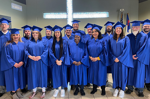 A group picture of smiling graduates in blue graduation gowns.