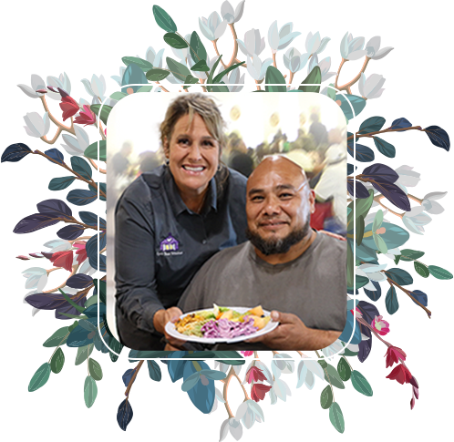 Image of Candace and a guest with a meal.  beautiful display of flowers are in in the background.